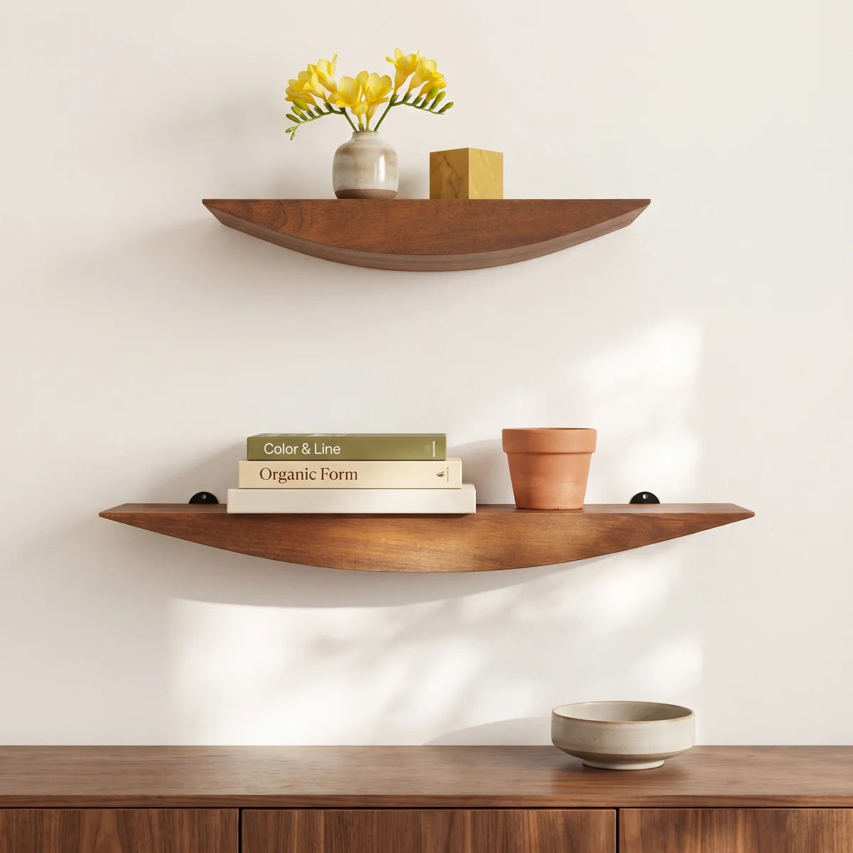 Oiva curved walnut shelves above a sideboard with flowers and books